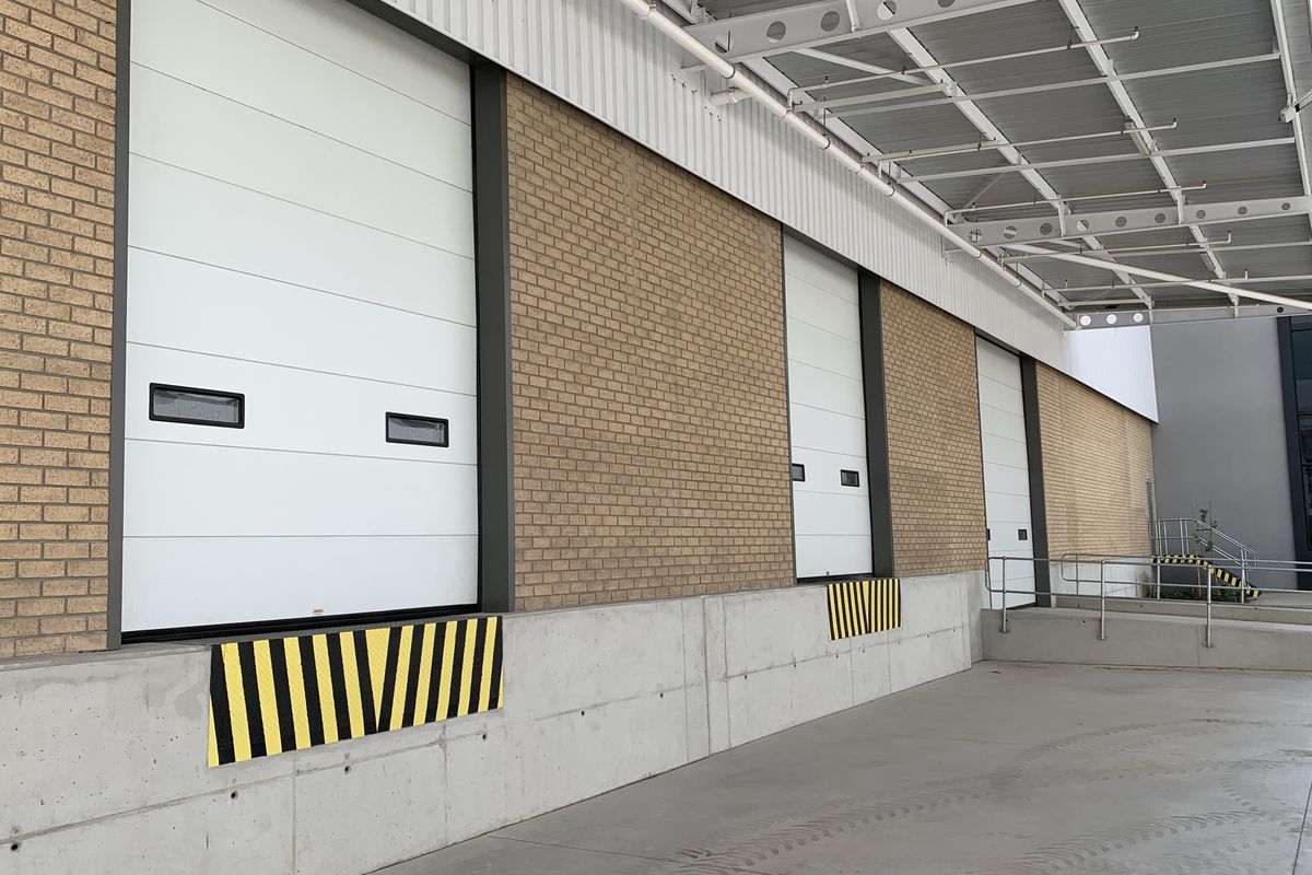Industrial loading bay area featuring multiple roller shutter doors, a concrete loading dock with safety bumpers, and a protective metal canopy.