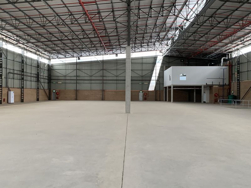 Spacious industrial warehouse featuring high ceilings with exposed steel trusses, polished concrete flooring, and an integrated mezzanine level for versatile operational use.
