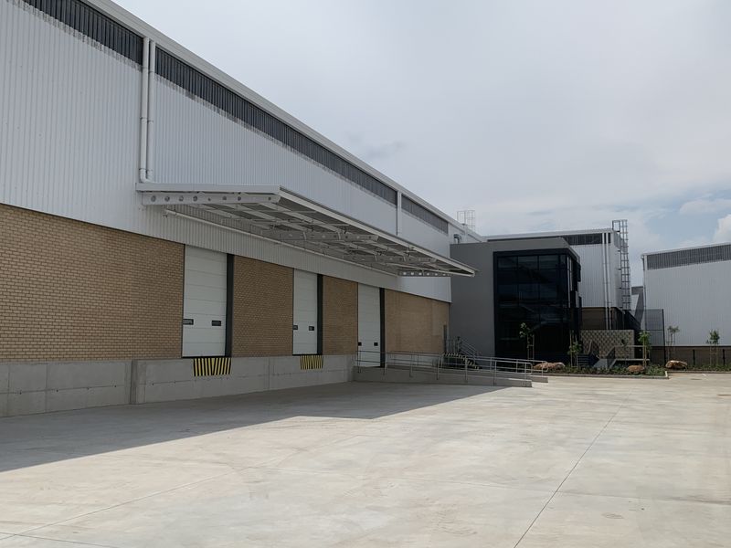 Industrial warehouse exterior featuring multiple loading docks with roller shutter doors, concrete hardstand area, and modern metal and brick facade construction.