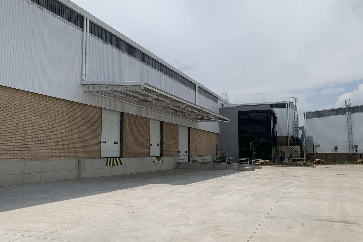 Industrial warehouse exterior featuring multiple loading docks with roller shutter doors, concrete hardstand area, and modern metal and brick facade construction.