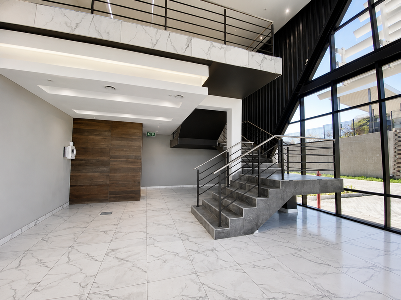 Modern industrial-style entrance foyer featuring high ceilings, a striking metal staircase, marble-look flooring, and expansive floor-to-ceiling windows providing abundant natural light.