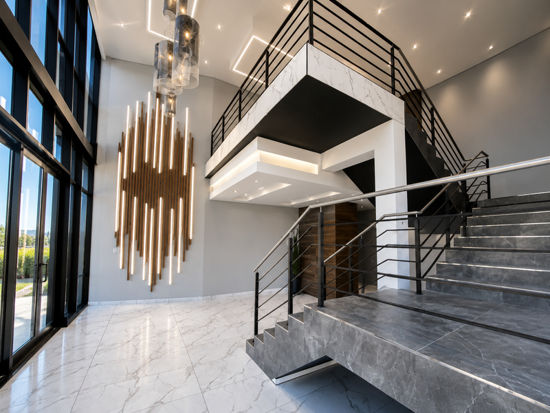 Grand double-volume entrance hall featuring floor-to-ceiling windows, a striking floating staircase with stone treads, and modern integrated lighting design.