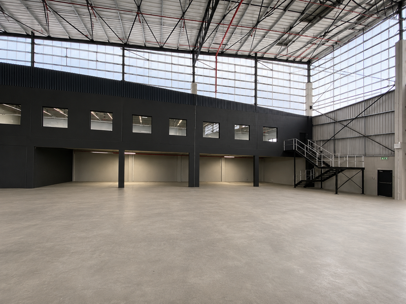 Spacious industrial warehouse interior featuring polished concrete floors, a mezzanine level with metal staircase, and high-clearance ceilings with integrated fire safety systems.
