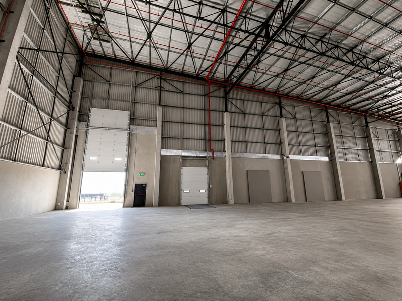 Spacious industrial warehouse featuring high ceilings with exposed steel trusses, concrete flooring, fire sprinkler system, and multiple roller shutter doors for efficient access.