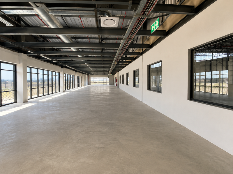 Spacious open-plan industrial office area featuring polished concrete floors, exposed steel ceiling structure, and extensive natural light through large aluminium-framed windows.