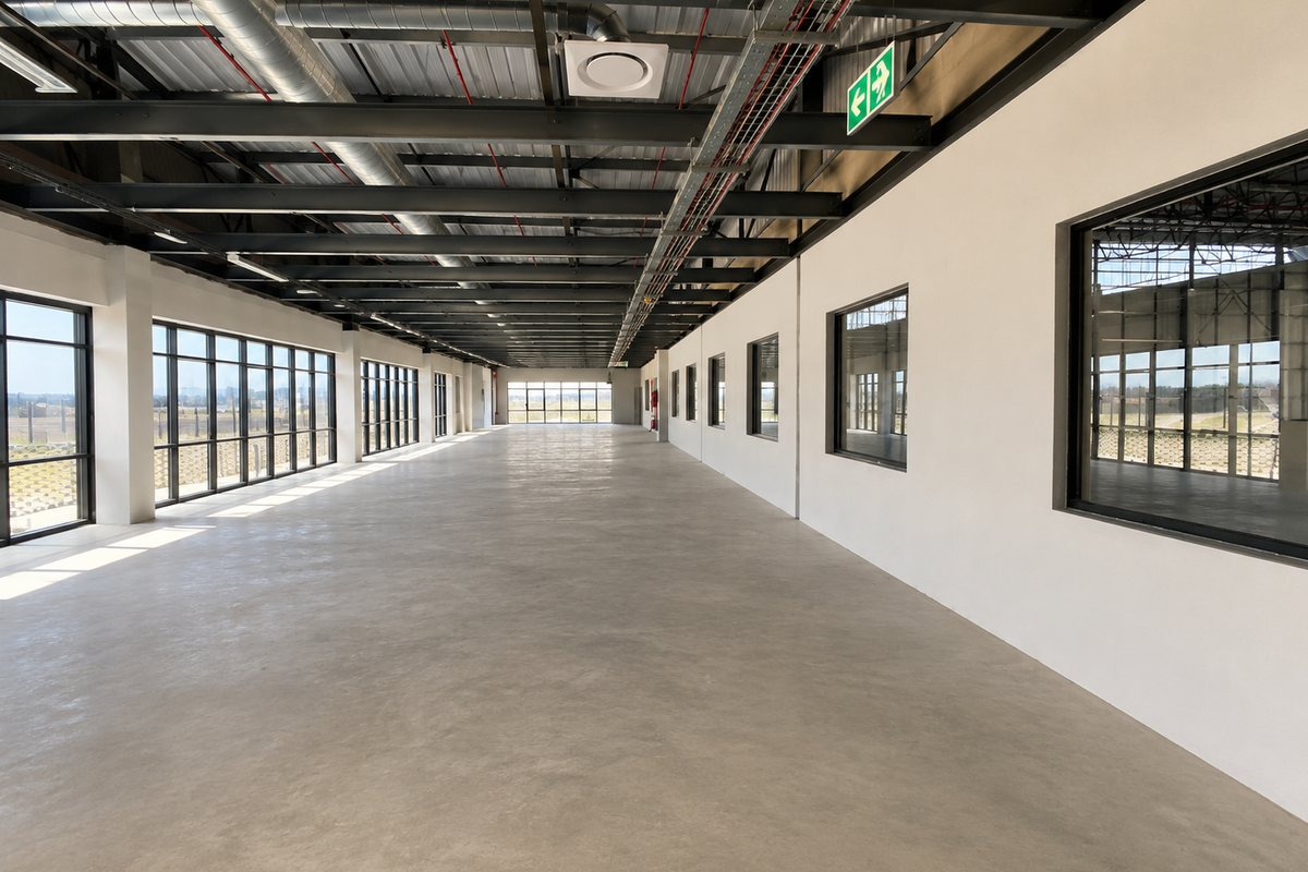 Spacious open-plan industrial office area featuring polished concrete floors, exposed steel ceiling structure, and extensive natural light through large aluminium-framed windows.