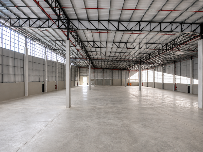 Spacious industrial warehouse featuring high ceilings with exposed steel trusses, polished concrete flooring, and extensive natural light through clerestory windows.