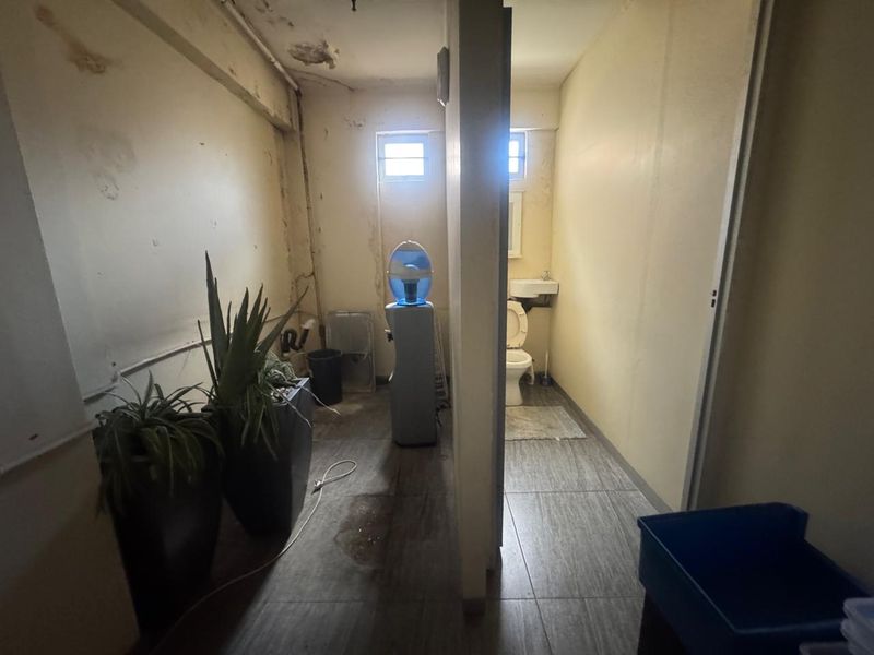 A utilitarian space featuring a small bathroom with a toilet and basin, showing signs of significant ceiling and wall wear requiring maintenance.