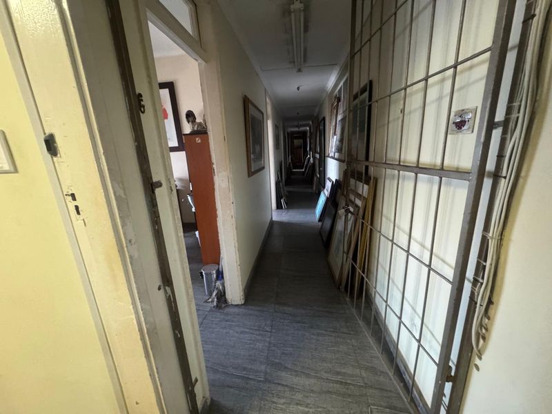 A long interior hallway featuring tiled flooring, fluorescent lighting, and a metal security gate, providing access to multiple rooms within the industrial property.
