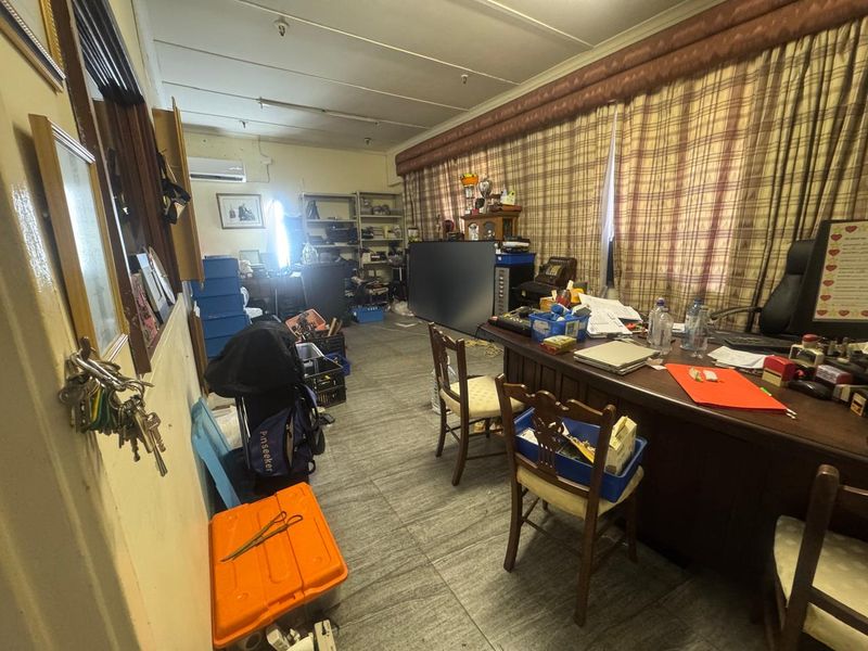 A functional office space featuring tiled flooring, wall-mounted air conditioning unit, and large window coverage, suitable for administrative or industrial management use.