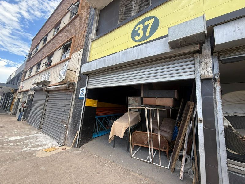 Industrial street-level unit featuring a metal roller shutter entrance, brick facade, and prominent signage, suitable for storage or workshop use.