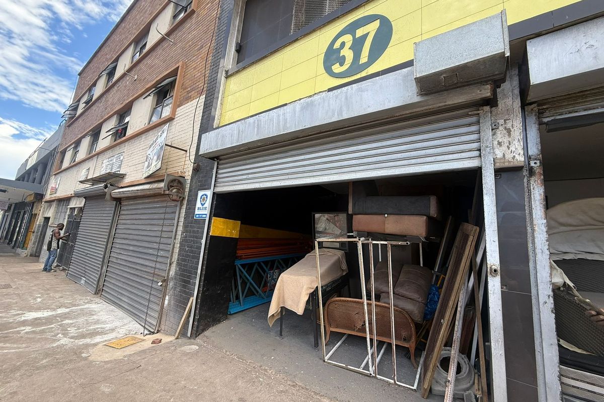 Industrial street-level unit featuring a metal roller shutter entrance, brick facade, and prominent signage, suitable for storage or workshop use.