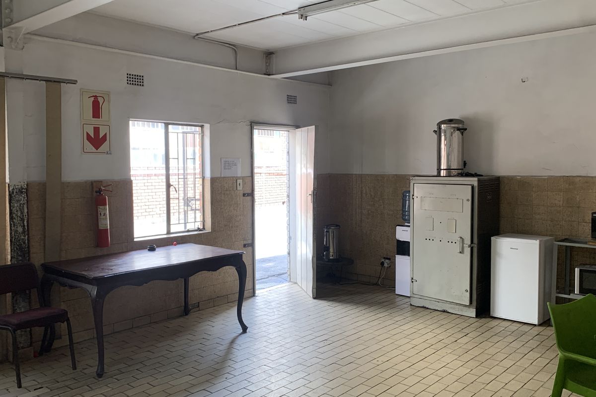 Functional industrial kitchen area featuring tiled flooring, wall wainscoting, and security window bars, suitable for staff utility or breakroom use.