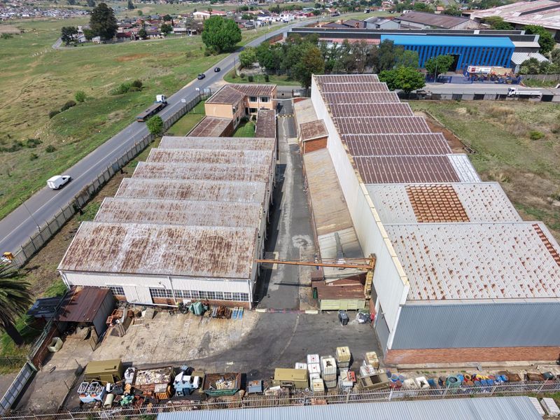 Aerial view of an industrial property featuring multiple warehouse buildings with corrugated metal roofing, a central yard area, and perimeter fencing.