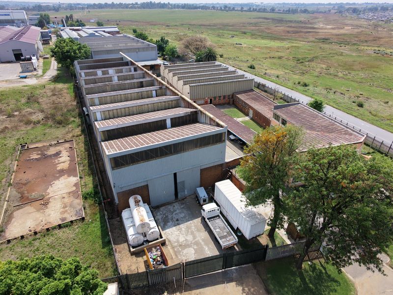 Aerial view of an industrial property featuring a large warehouse with a sawtooth roof, concrete yard, and perimeter fencing.