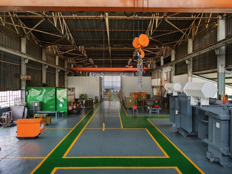 Spacious industrial workshop featuring high ceilings, exposed steel roof trusses, an overhead crane system, and durable painted concrete flooring with marked safety zones.