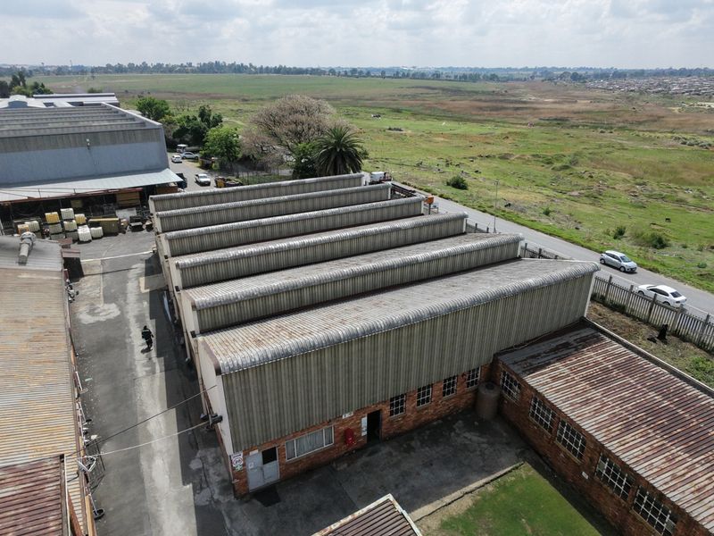 Aerial view of an industrial property featuring multiple sawtooth roof sections, brick exterior walls, and an adjacent asphalt driveway.