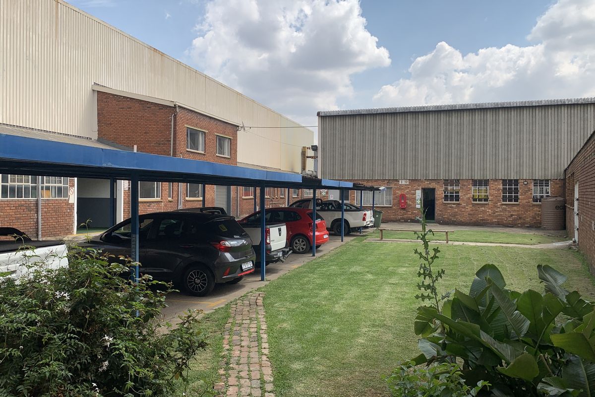 Rear industrial yard featuring a covered parking area, brick building facades, and a small landscaped lawn with a paved walkway.