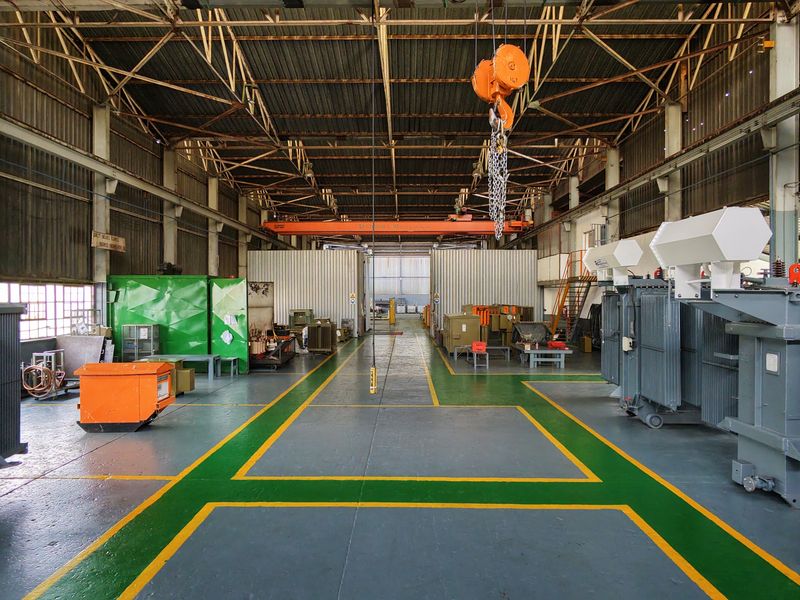 Spacious industrial workshop featuring high ceilings, exposed steel roof trusses, an overhead crane system, and durable painted flooring with marked work zones.