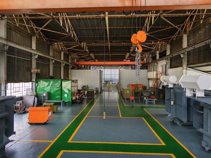 Spacious industrial workshop featuring high ceilings, an overhead crane system, and durable painted flooring, suitable for heavy-duty manufacturing or equipment maintenance operations.