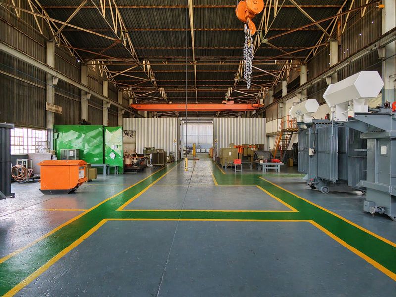 Spacious industrial workshop featuring high ceilings, overhead crane infrastructure, and durable painted flooring, suitable for heavy machinery maintenance and operations.