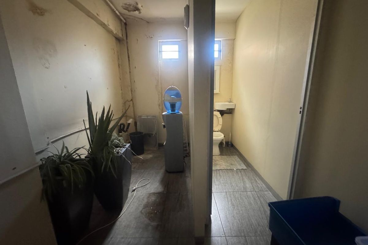A utilitarian space featuring a small bathroom with a toilet and basin, showing signs of significant ceiling and wall wear requiring maintenance.