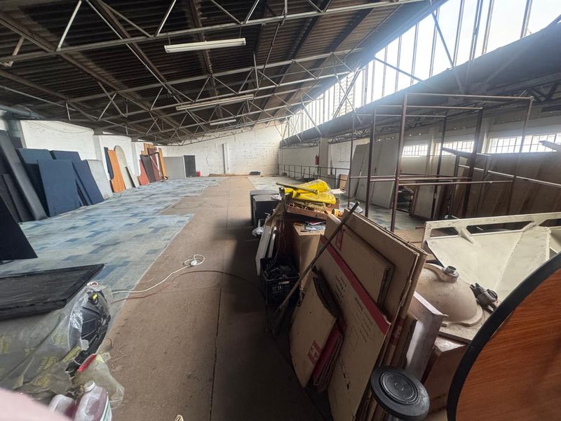 Spacious industrial warehouse area featuring high vaulted ceilings with exposed steel trusses, clerestory windows, and concrete flooring, suitable for storage or workshop use.