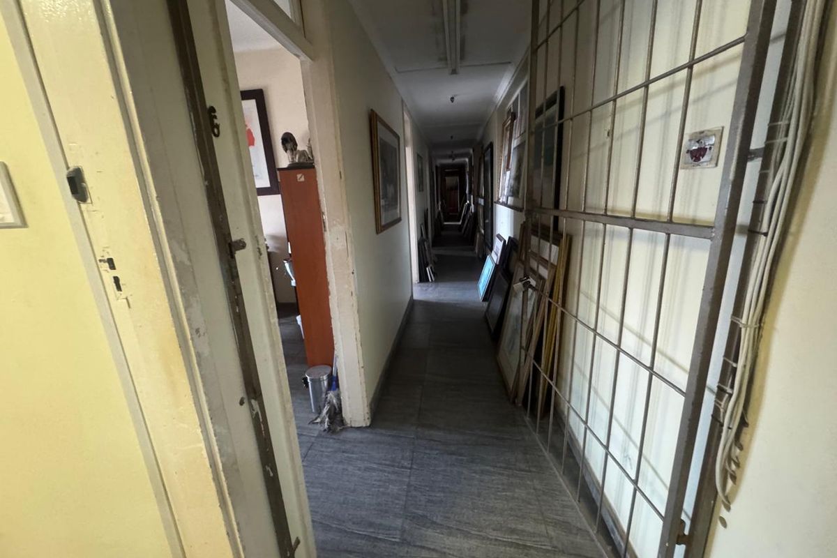A long interior hallway featuring tiled flooring, fluorescent lighting, and a metal security gate, providing access to multiple rooms within the industrial property.