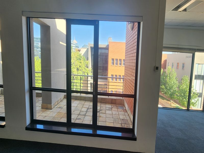 An empty office space featuring large glass sliding doors that open onto a private balcony with stone tiling and metal railings.