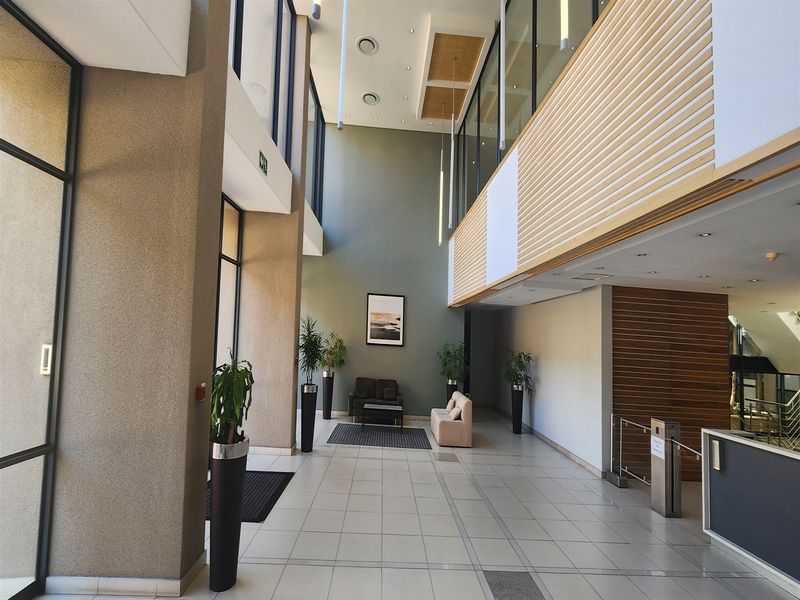 Spacious modern office building entrance lobby featuring double volume ceilings, large glass windows, tiled floors, and contemporary timber slat wall detailing.