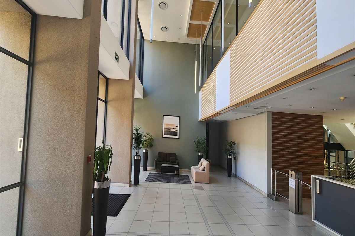 Spacious modern office building entrance lobby featuring double volume ceilings, large glass windows, tiled floors, and contemporary timber slat wall detailing.