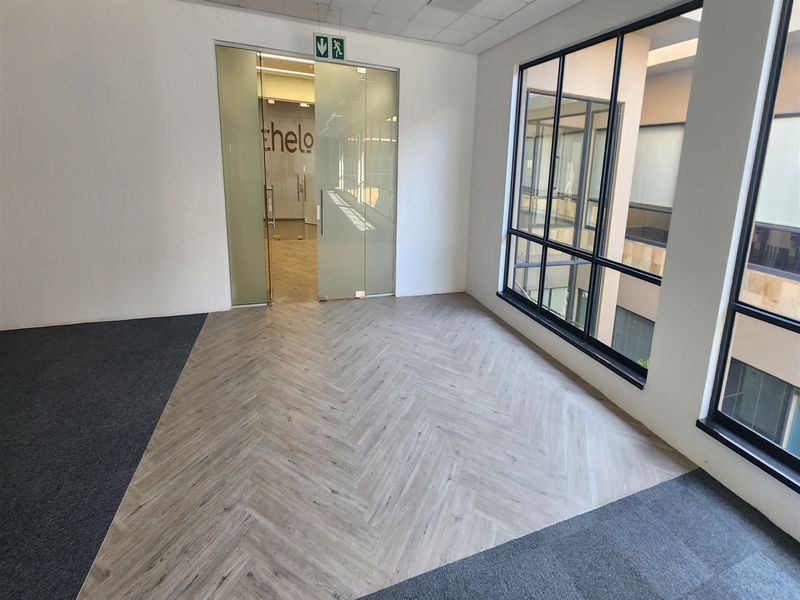 A bright, empty office space featuring modern herringbone vinyl flooring, carpet accents, and large windows overlooking an internal courtyard.