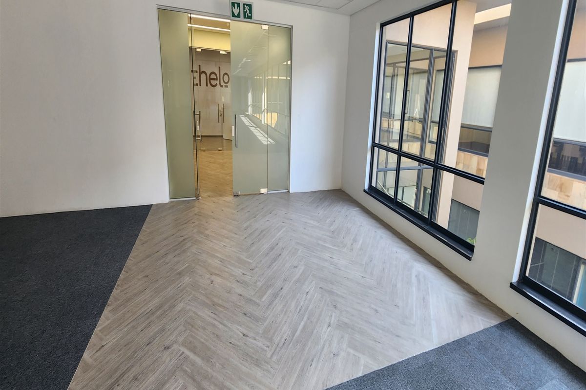 A bright, empty office space featuring modern herringbone vinyl flooring, carpet accents, and large windows overlooking an internal courtyard.