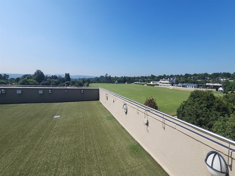A spacious rooftop terrace featuring artificial turf, stainless steel railings, and wall-mounted lighting, offering expansive views over the surrounding landscape.