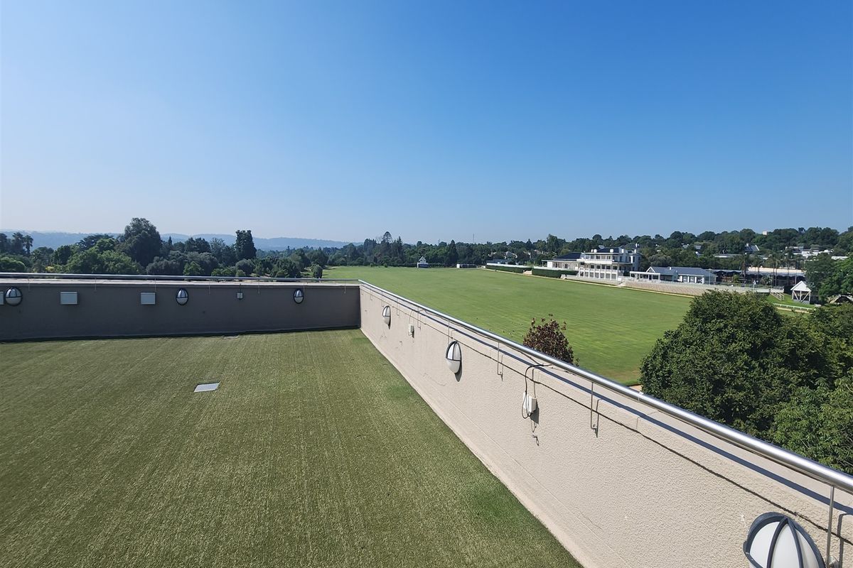 A spacious rooftop terrace featuring artificial turf, stainless steel railings, and wall-mounted lighting, offering expansive views over the surrounding landscape.
