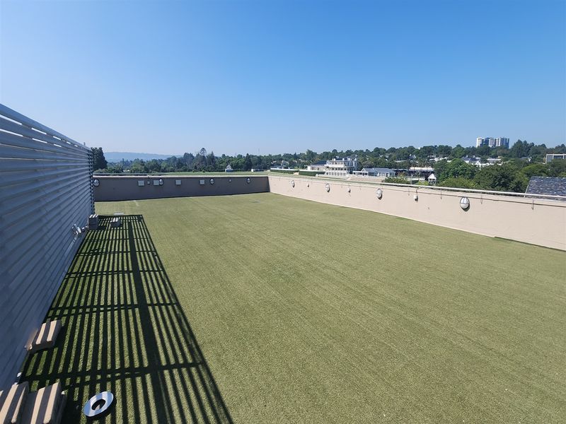 Spacious rooftop terrace featuring artificial turf, perimeter wall lighting, and a metal privacy screen, offering expansive views of the surrounding area.