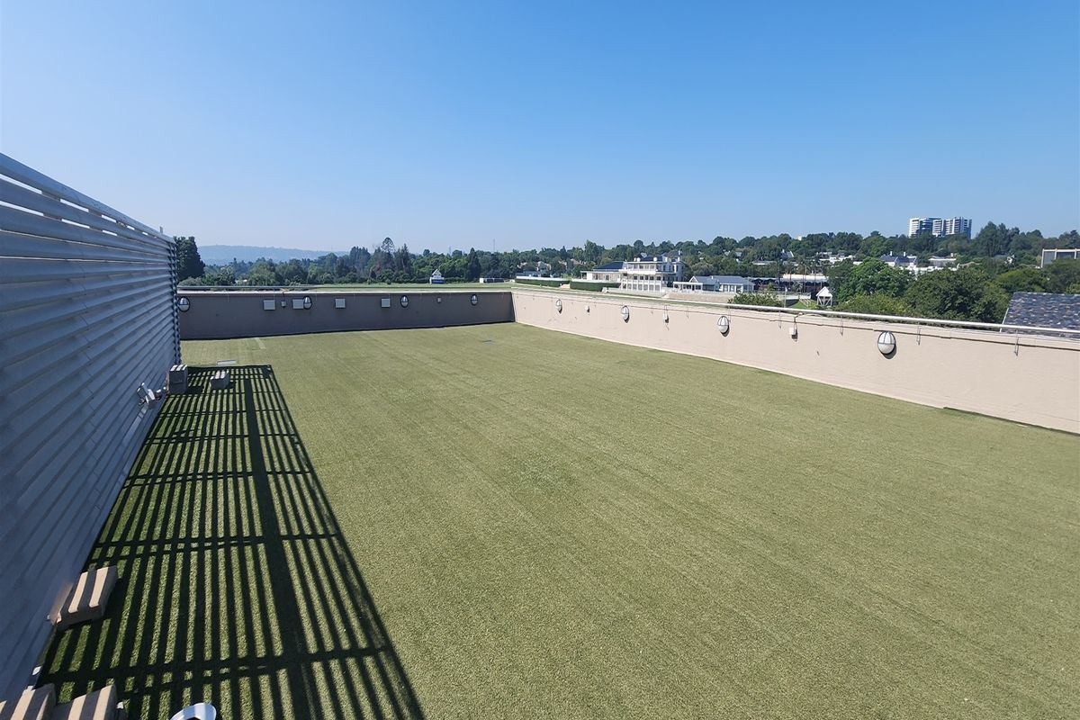 Spacious rooftop terrace featuring artificial turf, perimeter wall lighting, and a metal privacy screen, offering expansive views of the surrounding area.