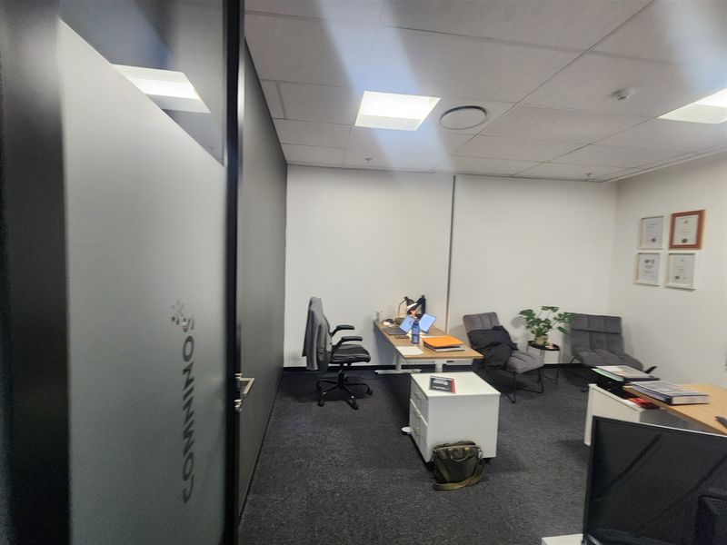 A functional office space featuring a suspended ceiling, recessed lighting, carpeted flooring, and a modern frosted glass partition entrance.