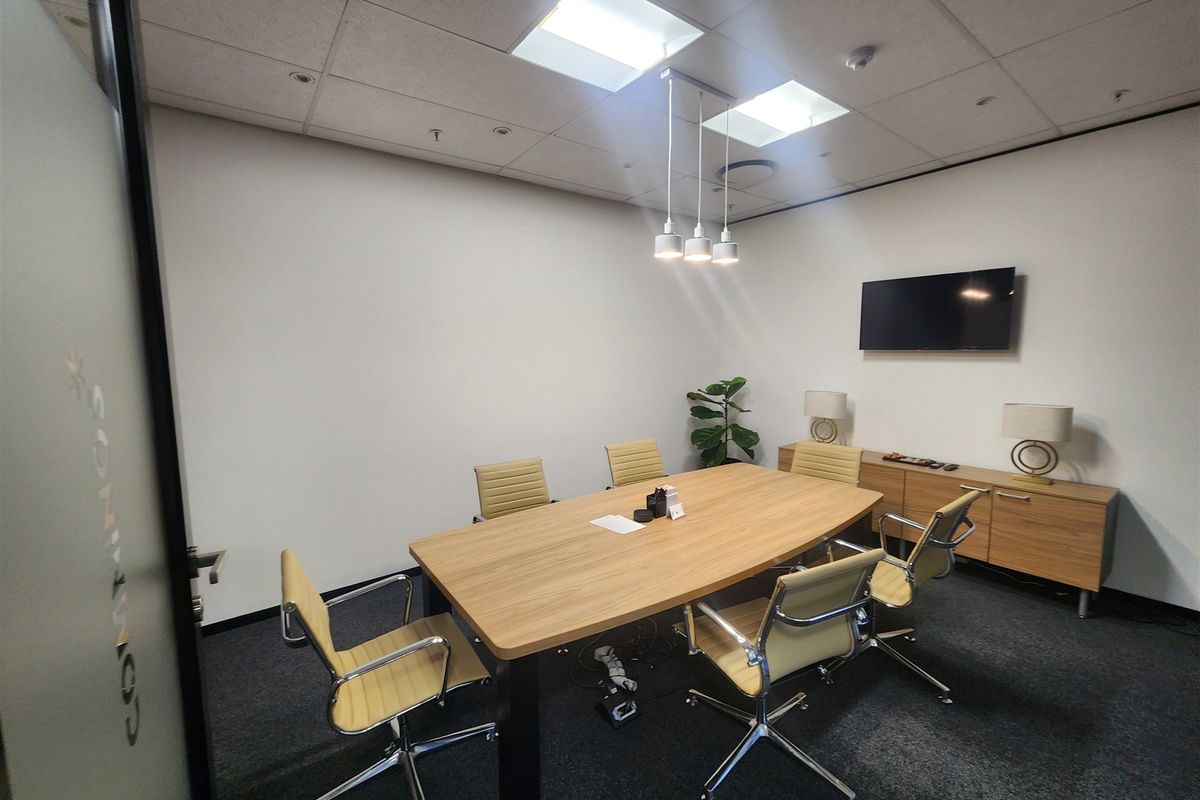 A professional meeting room featuring a suspended ceiling, recessed and pendant lighting, and carpeted flooring.