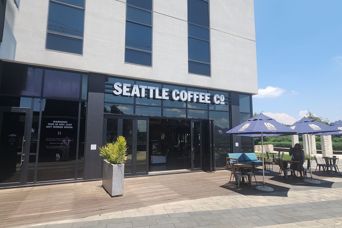 Modern commercial office building entrance featuring a glass facade, timber decking, and an outdoor seating area.
