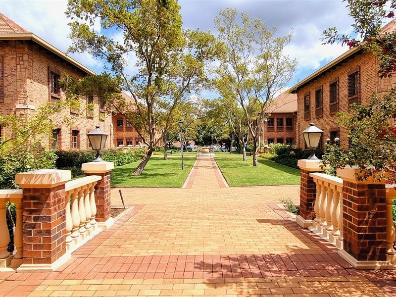 A well-maintained office complex courtyard featuring a central paved walkway, manicured lawns, mature trees, and classic brick architecture with decorative balustrades.