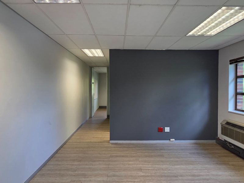 A clean, empty office space featuring modern laminate flooring, a suspended ceiling with recessed lighting, and a wall-mounted HVAC unit.
