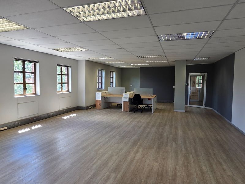 Spacious open-plan office area featuring laminate flooring, suspended ceilings with recessed lighting, and large windows providing natural light.