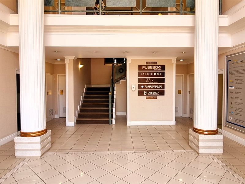 Spacious office building entrance lobby featuring decorative columns, a central staircase, and a directory board for multiple tenants.