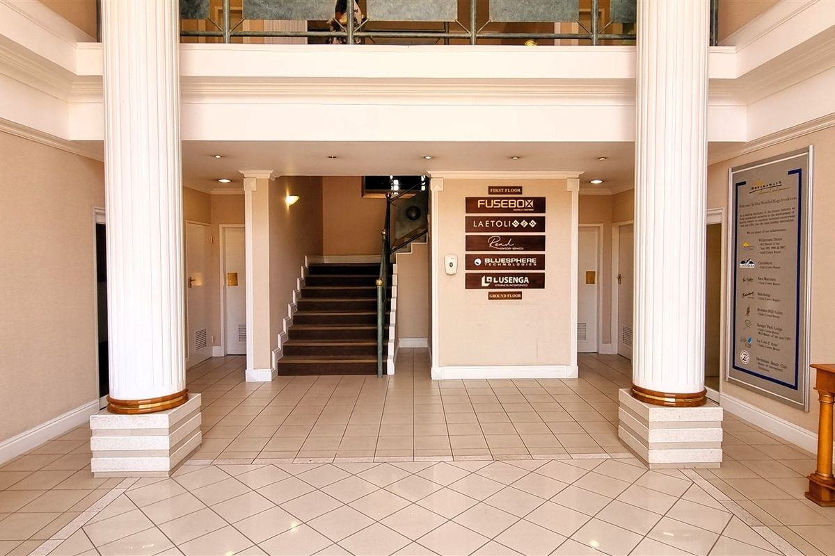 Spacious office building entrance lobby featuring decorative columns, a central staircase, and a directory board for multiple tenants.