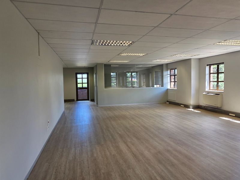 Spacious, open-plan office area featuring laminate flooring, a suspended ceiling with recessed lighting, and a wall-mounted air conditioning unit.