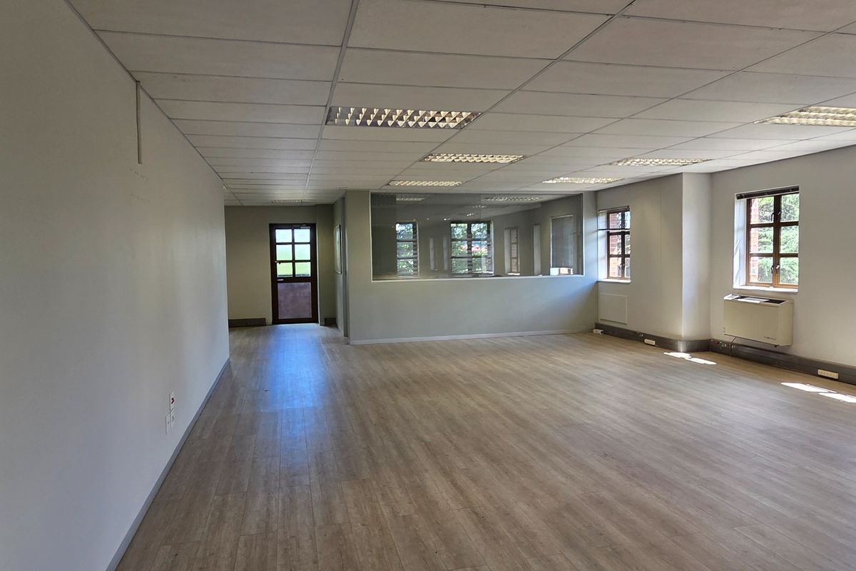 Spacious, open-plan office area featuring laminate flooring, a suspended ceiling with recessed lighting, and a wall-mounted air conditioning unit.