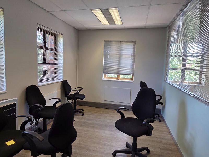 A functional office space featuring laminate flooring, recessed ceiling lighting, and multiple windows fitted with venetian blinds, providing a bright and professional work environment.