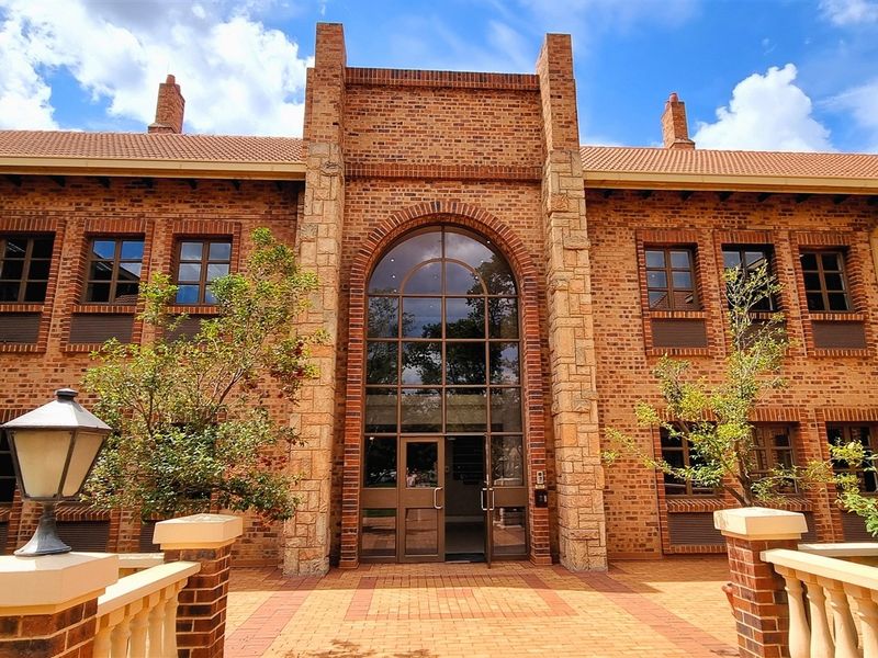 A well-maintained office building featuring a classic brick facade, stone-accented arched entrance, and a paved courtyard with decorative balustrades.