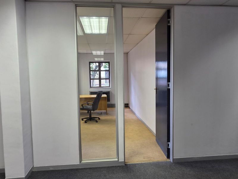 A vacant office space featuring a glass partition, suspended ceiling with recessed lighting, and carpeted flooring, offering a functional professional environment.